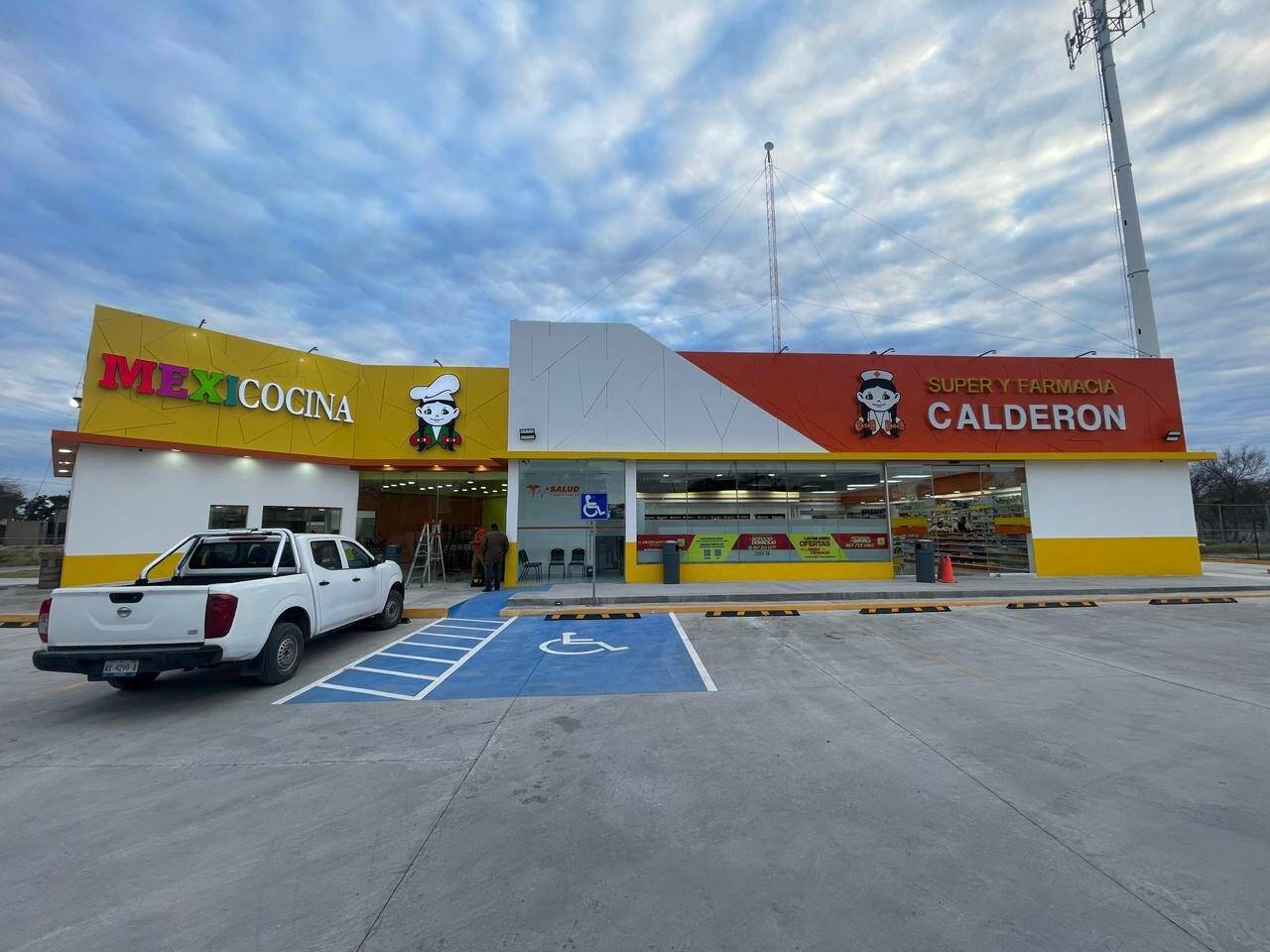 Fachada terminada de una Súper Farmacia Calderón con Mexicocina al lado, marquesina roja y blanca, zócalo amarillo y el estacionamiento trazado con cajón para persona con discapacidad.