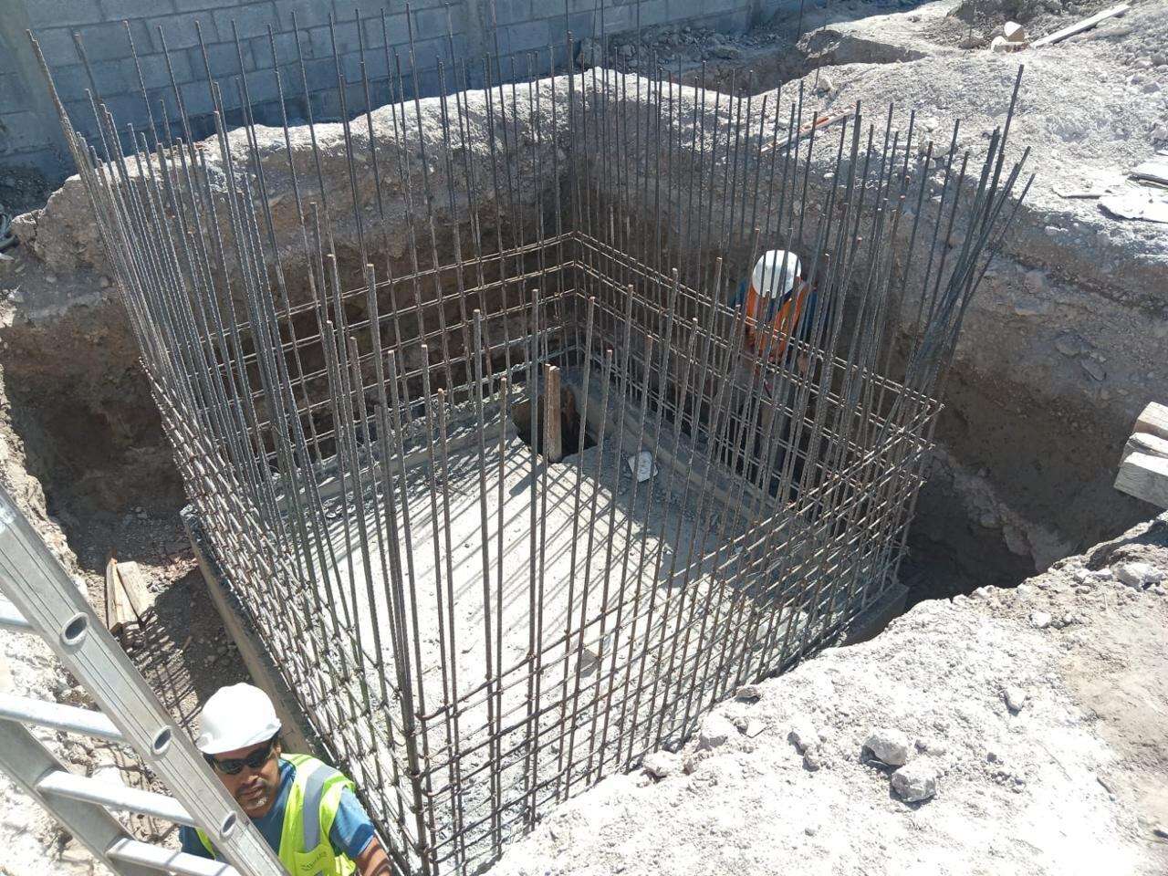 Excavación de una cisterna con los muros ya colados y cimbrados, una escalera de acceso al fondo y un trabajador con casco blanco y chaleco reflejante trabajando dentro.
