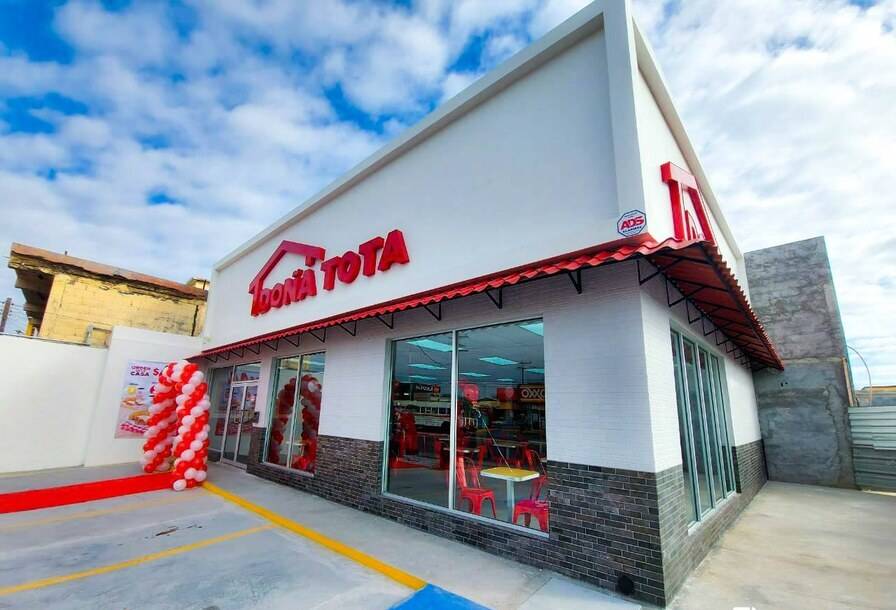 Fachada terminada de una sucursal de Doña Tota con marquesina roja y blanca, cortina de globos rojos y blancos en la entrada y el estacionamiento pintado con líneas amarillas y azules.