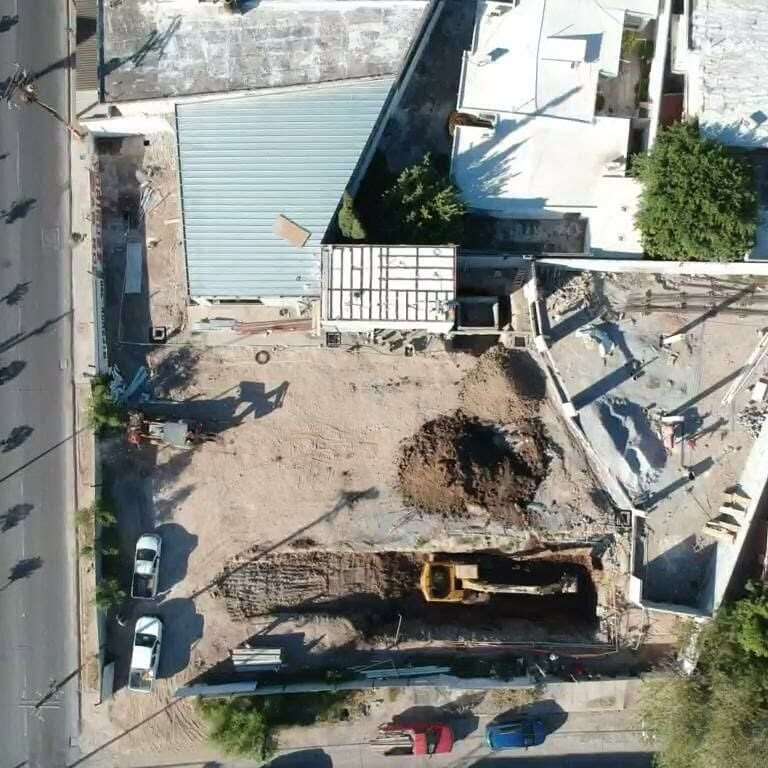 Vista aérea de una excavación en obra, con la máquina trabajando al fondo del corte y el terreno despalmado alrededor.