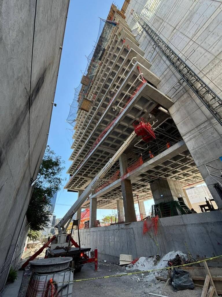 Estructura de un edificio en obra vista desde abajo, con la losa de entrepiso apuntalada, un elevador de carga rojo pegado a la fachada y el cielo despejado entre los niveles.
