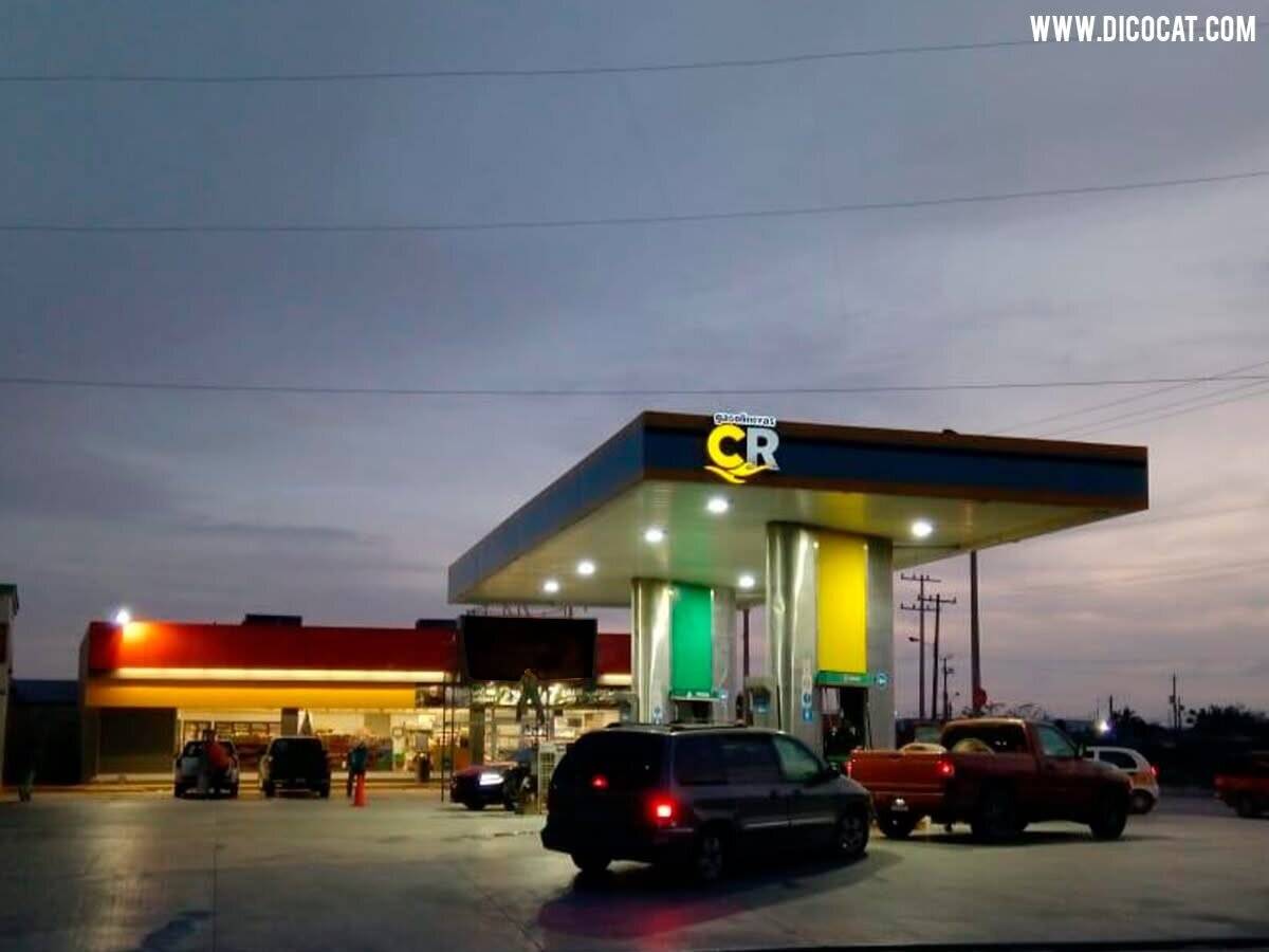 Estación de servicio de Gasolineras CR al anochecer, con la marquesina iluminada, las islas de despacho encendidas y vehículos cargando.