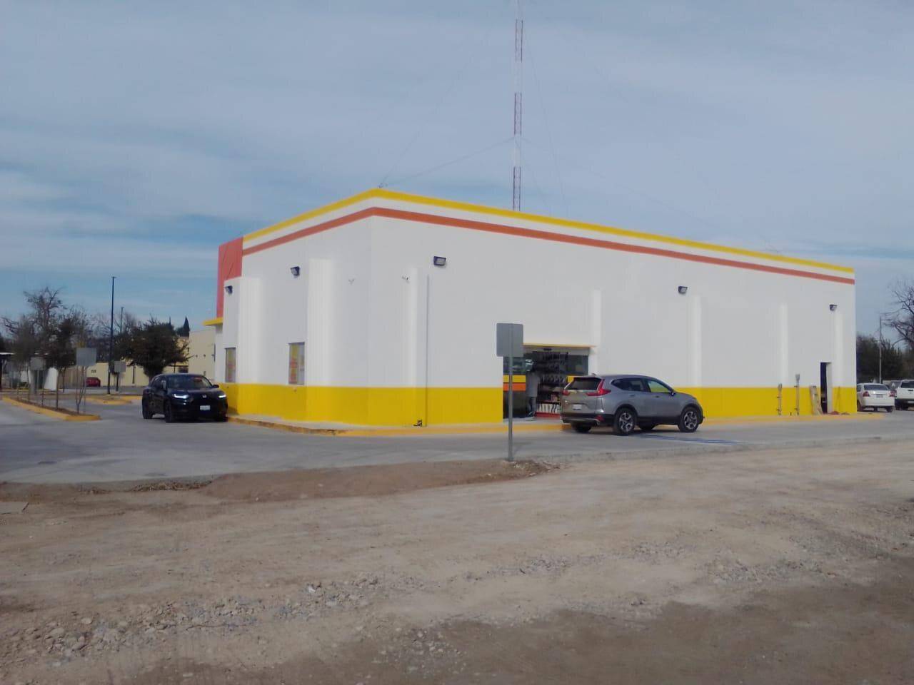 Local comercial terminado de muros blancos y zócalo amarillo, visto desde el estacionamiento vacío con una camioneta estacionada al frente.
