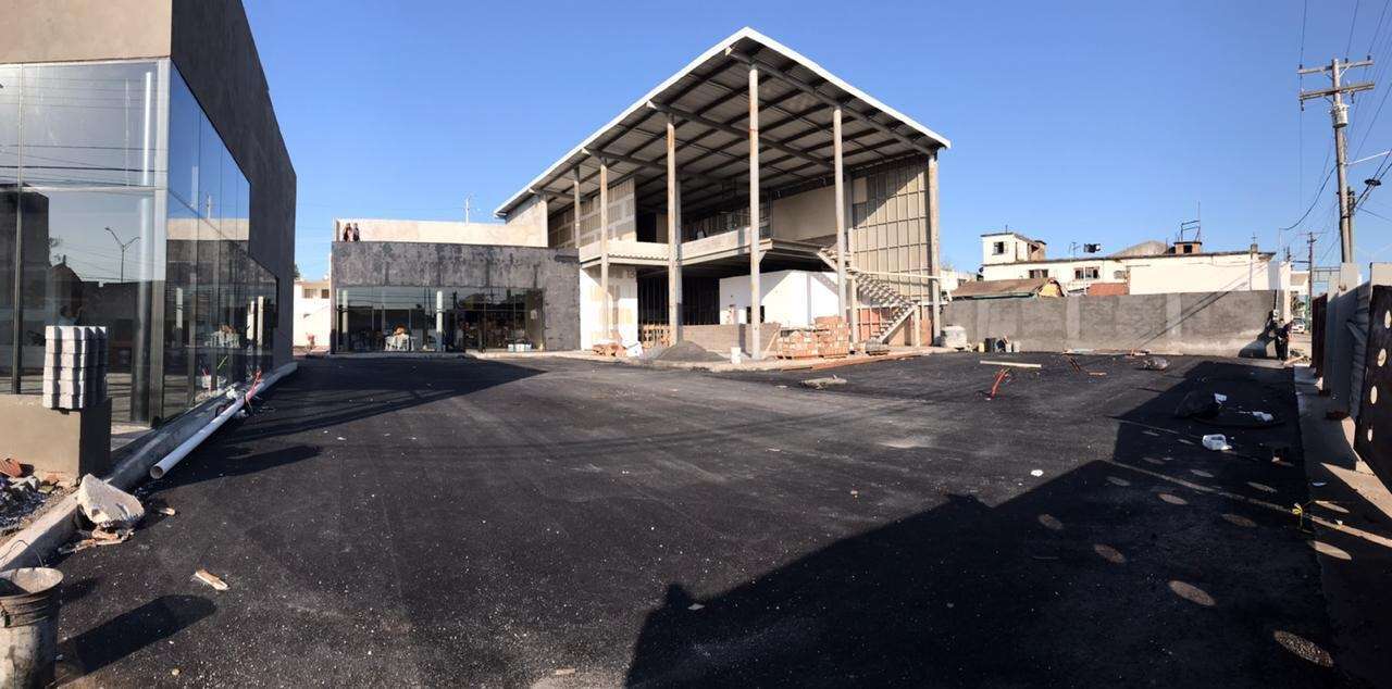 Nave comercial en obra con la estructura metálica y la cubierta montadas, junto a un local de cristal ya terminado y el patio recién asfaltado al frente.