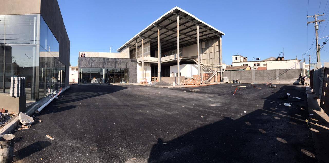 Nave comercial en obra con la estructura metálica y la cubierta montadas, junto a un local de cristal ya terminado y el patio recién asfaltado al frente.