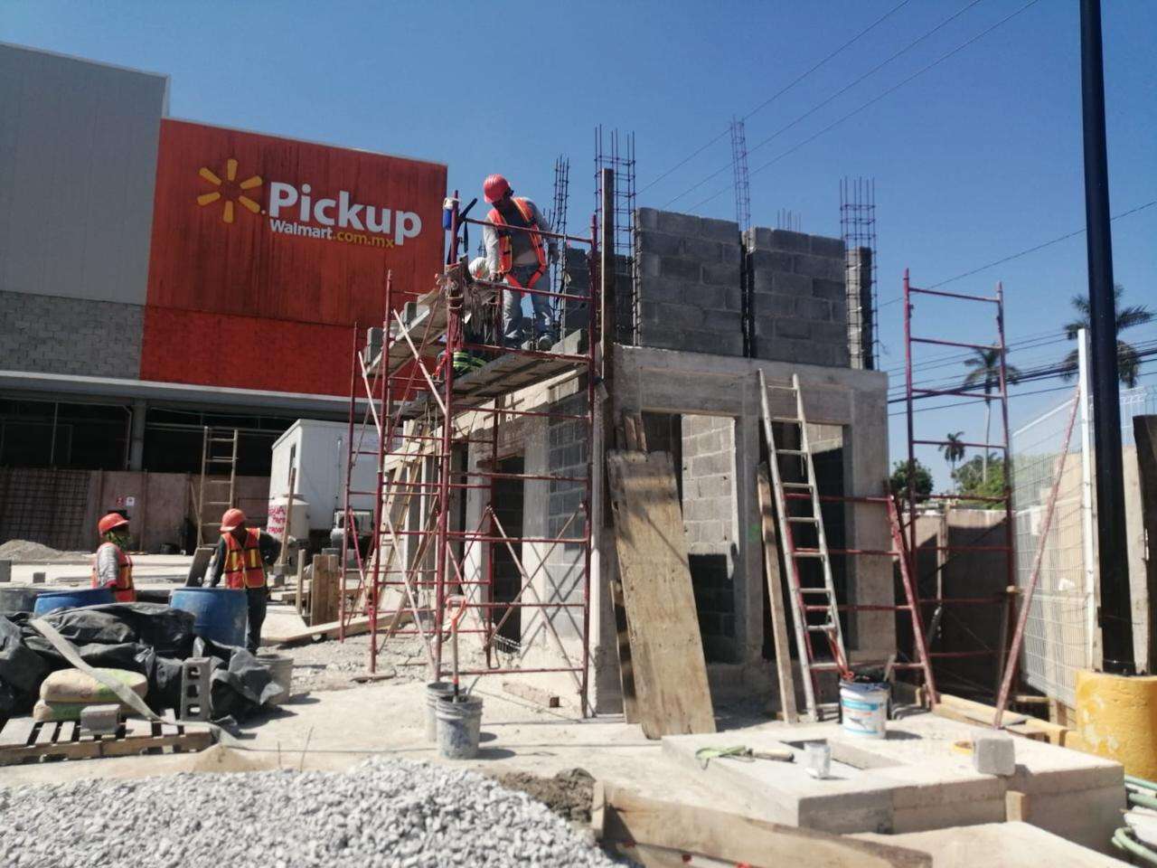 Obra de un local a pie de tienda, con andamios, muro de block a media altura, castillos armados y trabajadores con casco al frente.