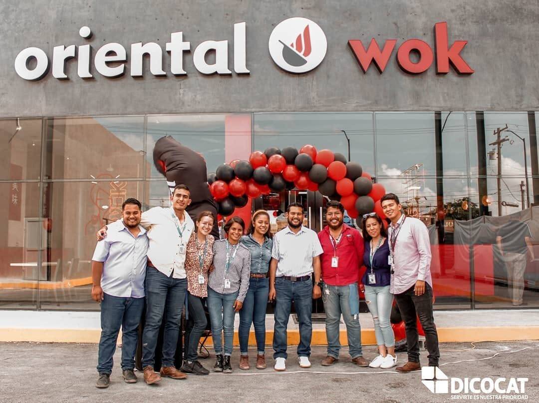 Grupo de personas frente a la fachada de Oriental Wok el día de la apertura, bajo un arco de globos negros y rojos.