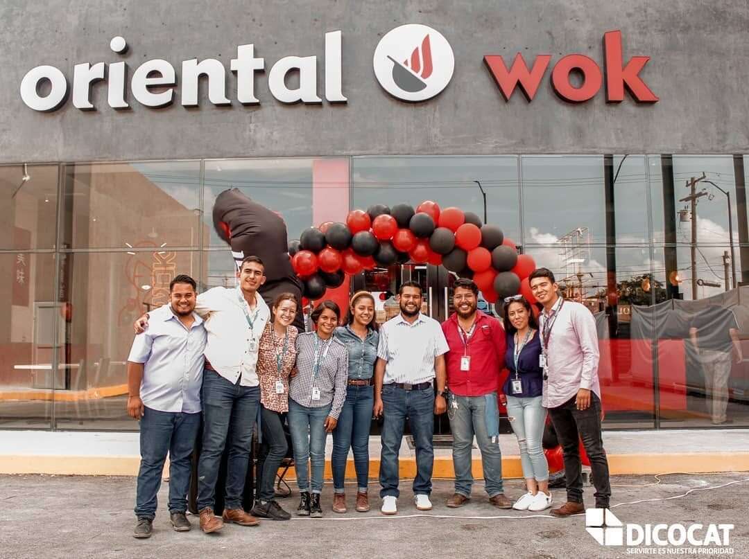 Grupo de personas frente a la fachada de Oriental Wok el día de la apertura, bajo un arco de globos negros y rojos.