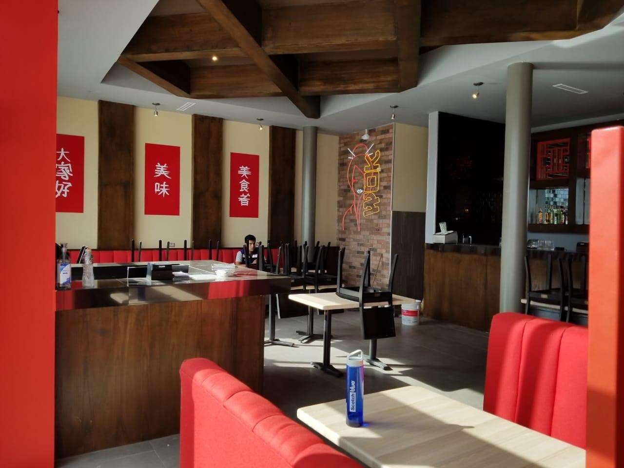 Interior terminado de un restaurante con plafón artesonado de madera, herrería roja, gabinetes y mesas con bancas rojas.