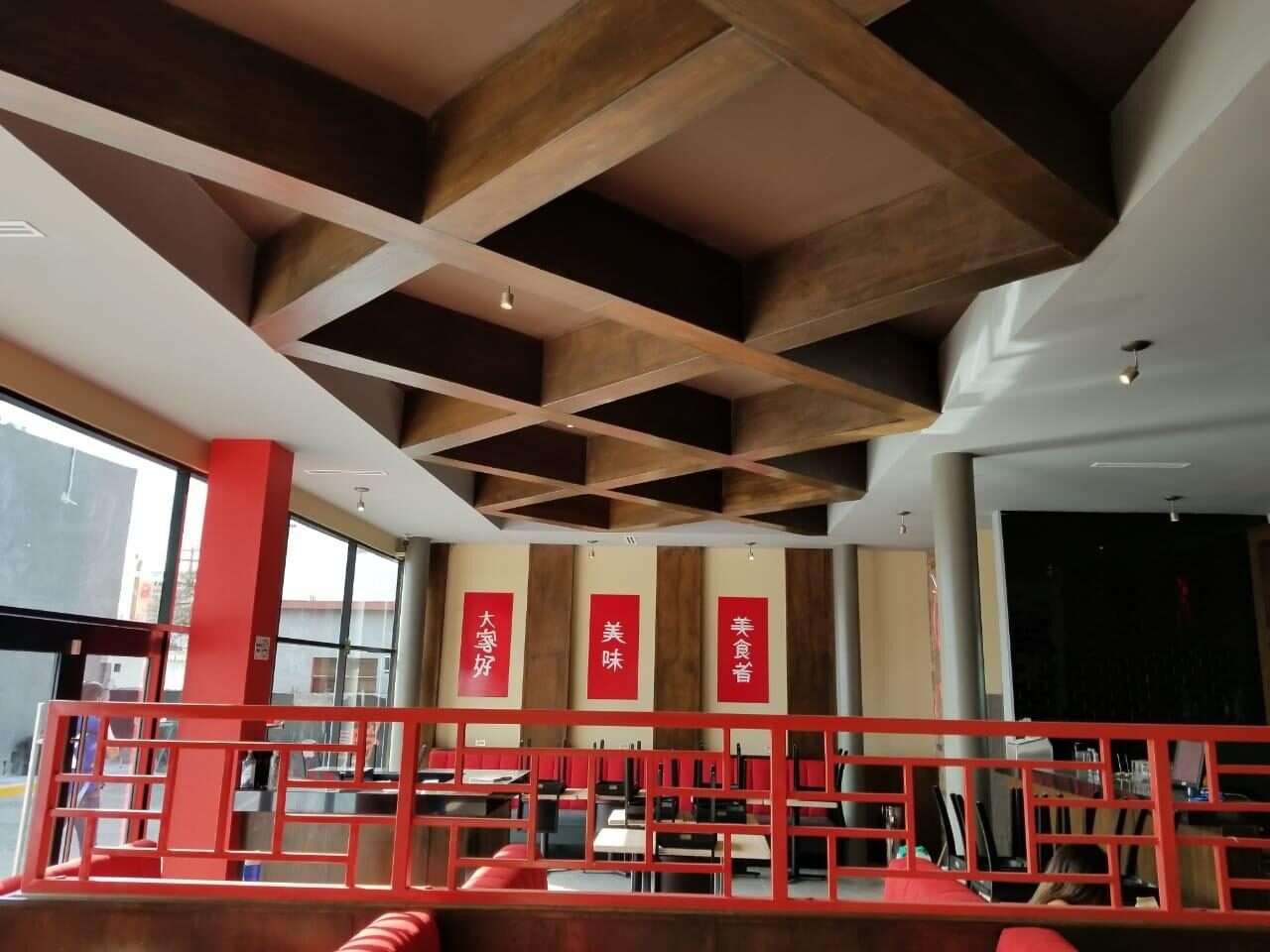 Entrepiso terminado de un restaurante, con plafón artesonado de madera, barandal de herrería roja y las mesas ya colocadas junto al ventanal.