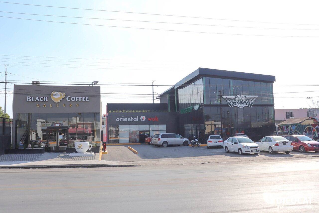 Conjunto comercial terminado visto desde la avenida, con los locales de Black Coffee, Oriental Wok y Wing Stop en línea y el estacionamiento al frente.