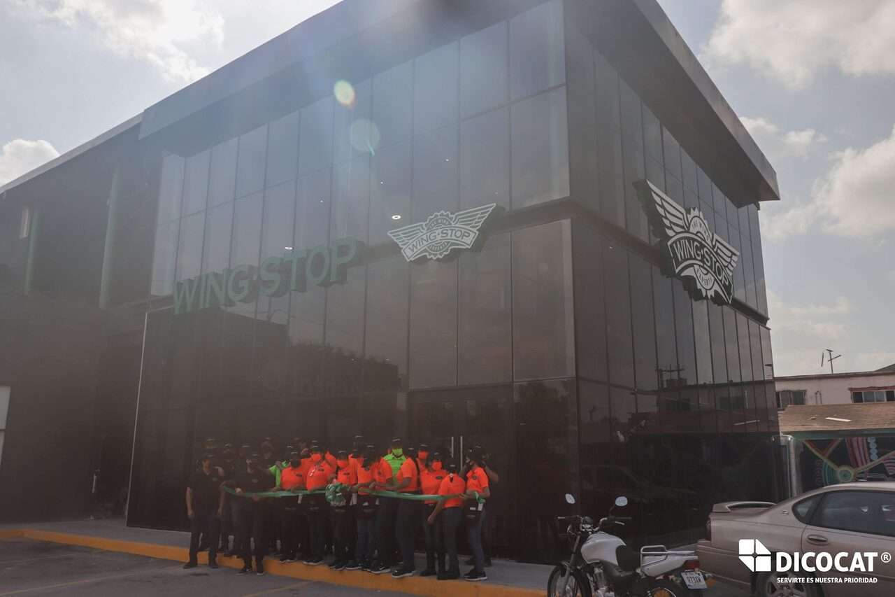 Personal formado frente al edificio de cristal de Wing Stop el día de la apertura, con el anuncio de letra volumétrica ya montado en la fachada.